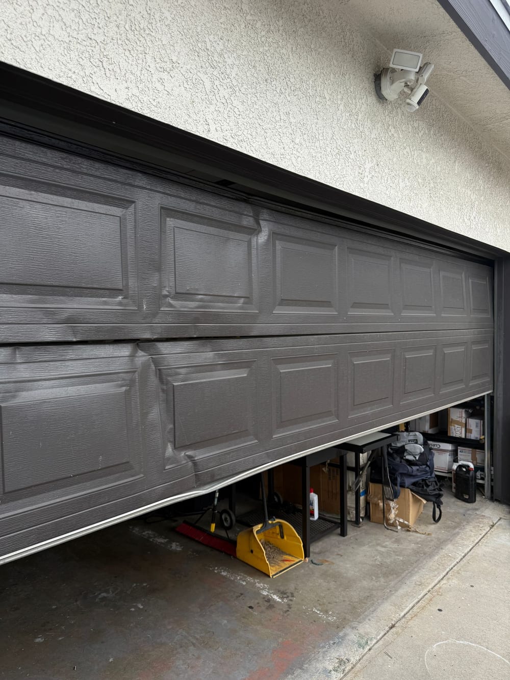 Dented brown steel garage door on a stucco house, its lower sections pushed out of line