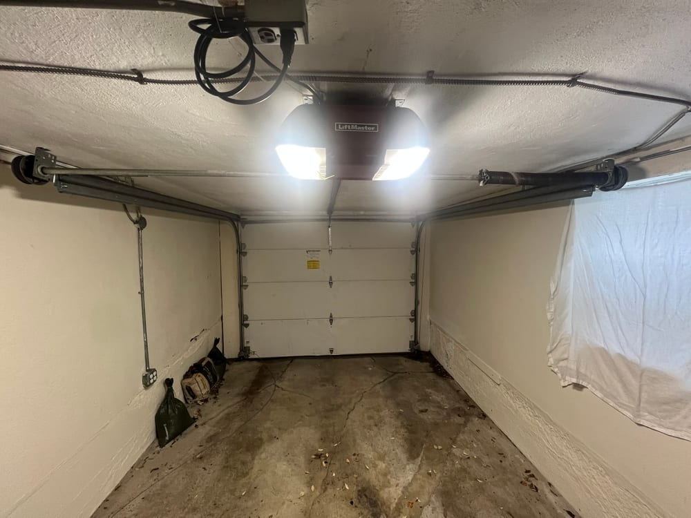 Garage door opener lit up on the ceiling of an empty garage, door closed